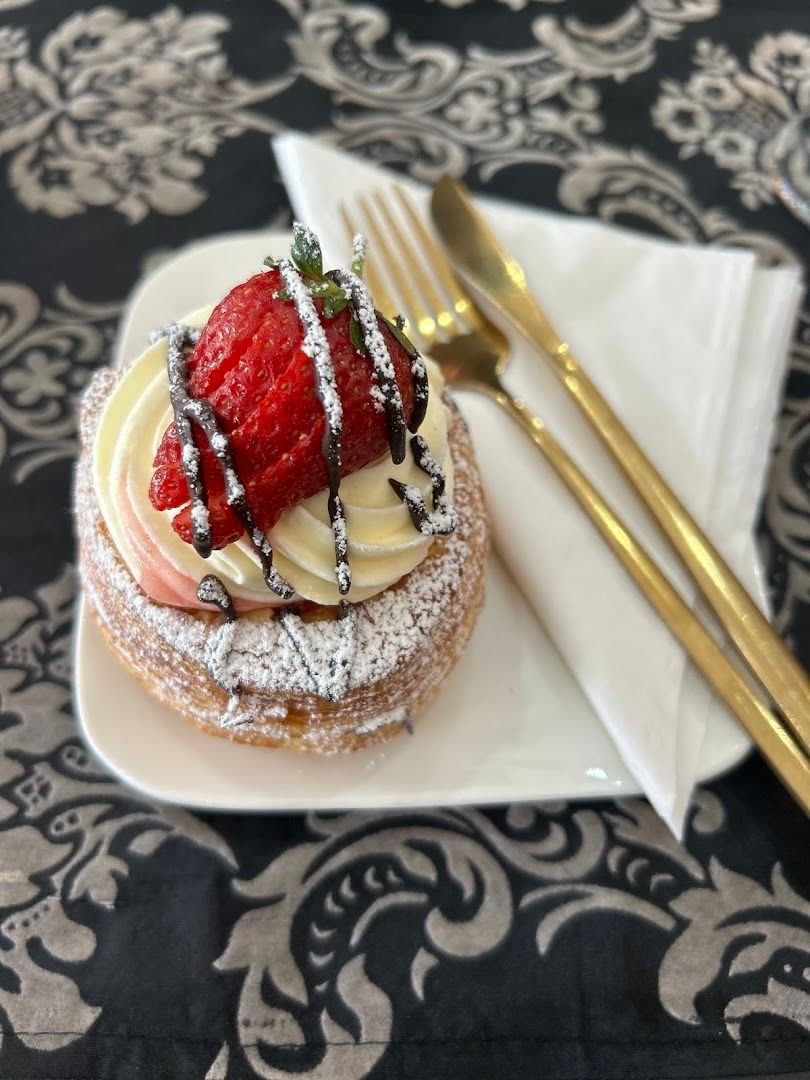 A strawberry and cream choux pastry with chocolate drizzle, served with gold cutlery